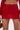 A close-up of a person in the FIERCE MESH MINI SKIRT, a sheer red mesh mini with a curve-hugging fit, styled with a matching feather-sleeve top and holding a brown textured handbag.