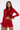 A woman stands against a plain light background with one hand on her hip, wearing the FIERCE FEATHER BLOUSE—a red, sheer mesh top with feather trim—paired with a matching red mini skirt.