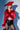 A confident woman poses against a blue and white background, wearing a FIERCE FEATHER BLOUSE with feather trim, black high-waisted shorts, a wide-brimmed red hat, and holding a red handbag.