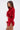 A woman stands in profile wearing the FIERCE FEATHER BLOUSE—a fitted, long-sleeve red crop top with a matching mini skirt, both detailed with red feather trim on the neckline, sleeves, and hem—set against a plain light background.