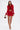 A woman poses in the FIERCE FEATHER BLOUSE, a red crop top with feather trim, paired with a matching mini skirt. She accessorizes with a leopard-print handbag and gold strappy heels against a plain background.