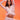 A woman with long dark hair and a serious expression raises her arms above her head while posing confidently in the ICY HOT FEATHER BLOUSE against a vibrant pink and orange gradient background.