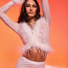 A woman with long dark hair and a serious expression raises her arms above her head while posing confidently in the ICY HOT FEATHER BLOUSE against a vibrant pink and orange gradient background.