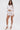 A woman models the ICY HOT FEATHER BLOUSE, a sheer mesh top with feather trim, and a matching mini skirt, styled with white heels against a plain white background.