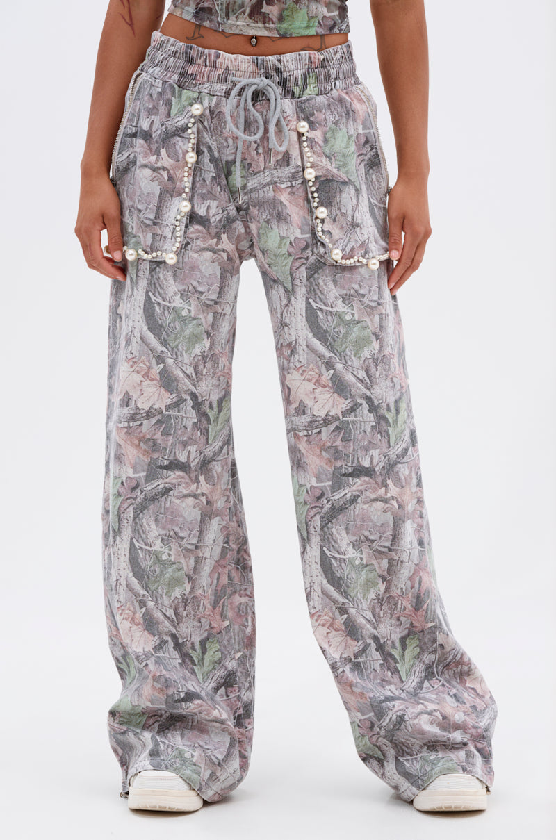 Someone stands against a plain white background wearing MEET ME HALFWAY WIDE LEG PANT, featuring a loose fit, abstract grey, green, and pink camo print, drawstring waist, and pearl-embellished front pockets. 1