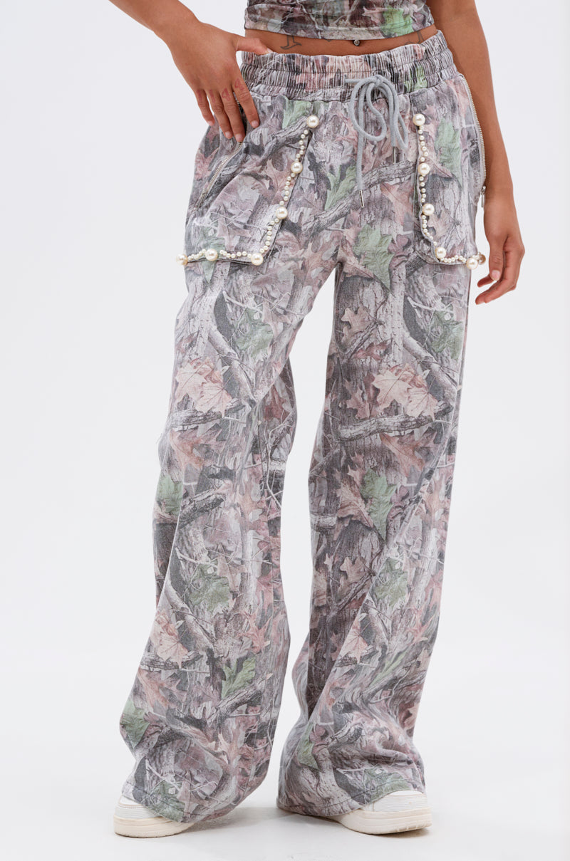 Wearing the MEET ME HALFWAY WIDE LEG PANT in muted camo with pearl-detailed front pockets, styled with white sneakers. The cropped, wide-leg cut offers a modern, casual vibe. 2
