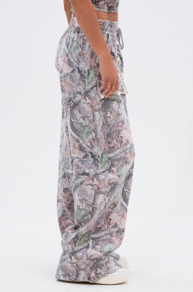 A person models the MEET ME HALFWAY WIDE LEG PANT in a camo print, paired with white sneakers. The high-waisted, loose fit and wide leg style give a relaxed edge as they stand sideways against a plain white background. 3