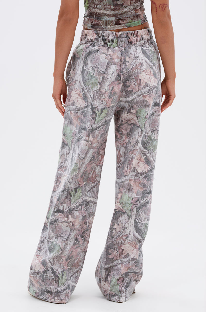 A person stands facing away, wearing the MEET ME HALFWAY WIDE LEG PANT—loose-fitting, high-waisted cargo pants with a gray, green, and brown leaf camo print and elastic waistband. 4