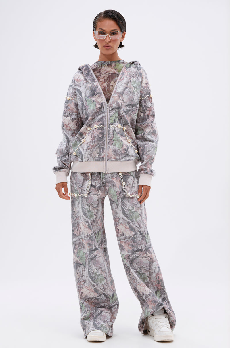 A person poses against a plain background wearing the MEET ME HALFWAY WIDE LEG PANT in gray and pastel floral print, paired with a matching hoodie over a sheer top, white sneakers, and translucent sunglasses. 7
