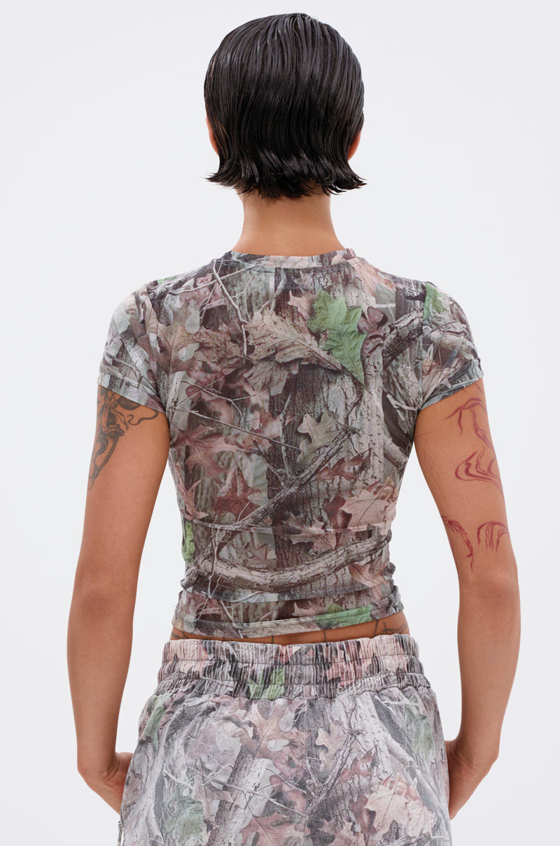 Person with short, wet-look dark hair and arm tattoos is seen from behind wearing the MEET ME HALFWAY PRINTED MESH TEE in a cropped camo print, paired with matching pants, against a plain light background.