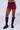 A person wearing the WHATEVER SHE WANTS MINI SKIRT, a short, dark pink mini skirt with black trim and a faux leather mock belt, stands with their legs slightly apart. They have on black, knee-high boots adorned with studs and multiple straps.