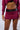 A person is wearing a cropped maroon sweatshirt and the "WHATEVER SHE WANTS MINI SKIRT," which features a high rise design and a faux leather mock belt. The image is focused from the shoulders to the lower thighs, against a plain light background.