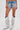 A person wears DIVALICIOUS DENIM SHORTS with beaded fringe and tall silver cowboy boots with fringe, standing against a plain white background.