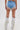 A person faces away, wearing DIVALICIOUS DENIM SHORTS with pearl fringe trim and sparkly white Western-style fringe cowboy boots against a plain white background.