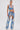 A woman poses against a white background in the DIVALICIOUS DENIM SHORT, a unique Western-inspired outfit with a sleeveless crop top and high-waisted chaps-style shorts accented by silver embroidery, rhinestones, beads, and fringe.