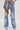A person wears DIVALICIOUS DENIM CHAPS IN LIGHT BLUE—jeans with one leg cut out to reveal beaded fringe shorts, rhinestone chain link fringe, silver embroidery, and sparkling bead details.