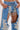 A person wears DIVALICIOUS DENIM CHAPS IN LIGHT BLUE featuring intricate silver floral patches, open at the front to reveal matching denim shorts accented with sparkling rhinestone chain link fringe.