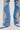 A close-up of legs wearing the DIVALICIOUS DENIM CHAPS IN LIGHT BLUE, featuring flared blue denim with silver bead and sequin floral designs, floral patches, pointed silver shoes, and sparkling rhinestone chain link fringe.