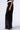 A person is standing against a plain background, donning the TRUE STORY SEQUIN PANT with its elasticized waistband. The high-rise wide-leg design features a shimmering finish, paired perfectly with black pointed-toe heels. Only the lower half of their body is visible.