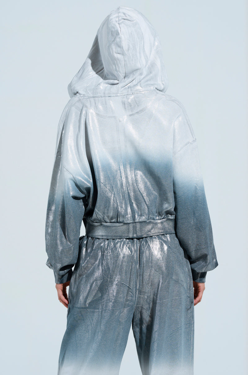 A person stands facing away, wearing an oversized fit of the "Shining Down on You" sweatshirt in a shiny silver and gray gradient against a light background. The loungewear reflects light, showcasing an iridescent appearance with a metallic finish.