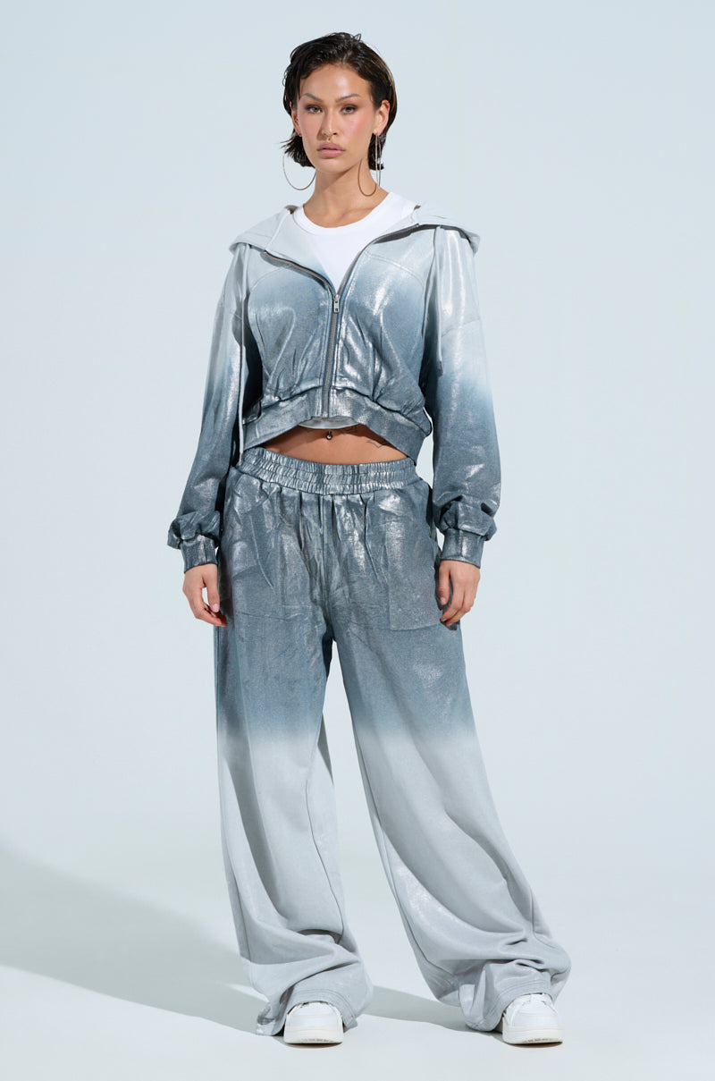 A person poses confidently in loungewear, showcasing the SHINING DOWN ON YOU SWEATSHIRT paired with matching loose-fitting pants. Their hands are in their pockets, highlighting the ensemble's metallic finish against a light grey background.