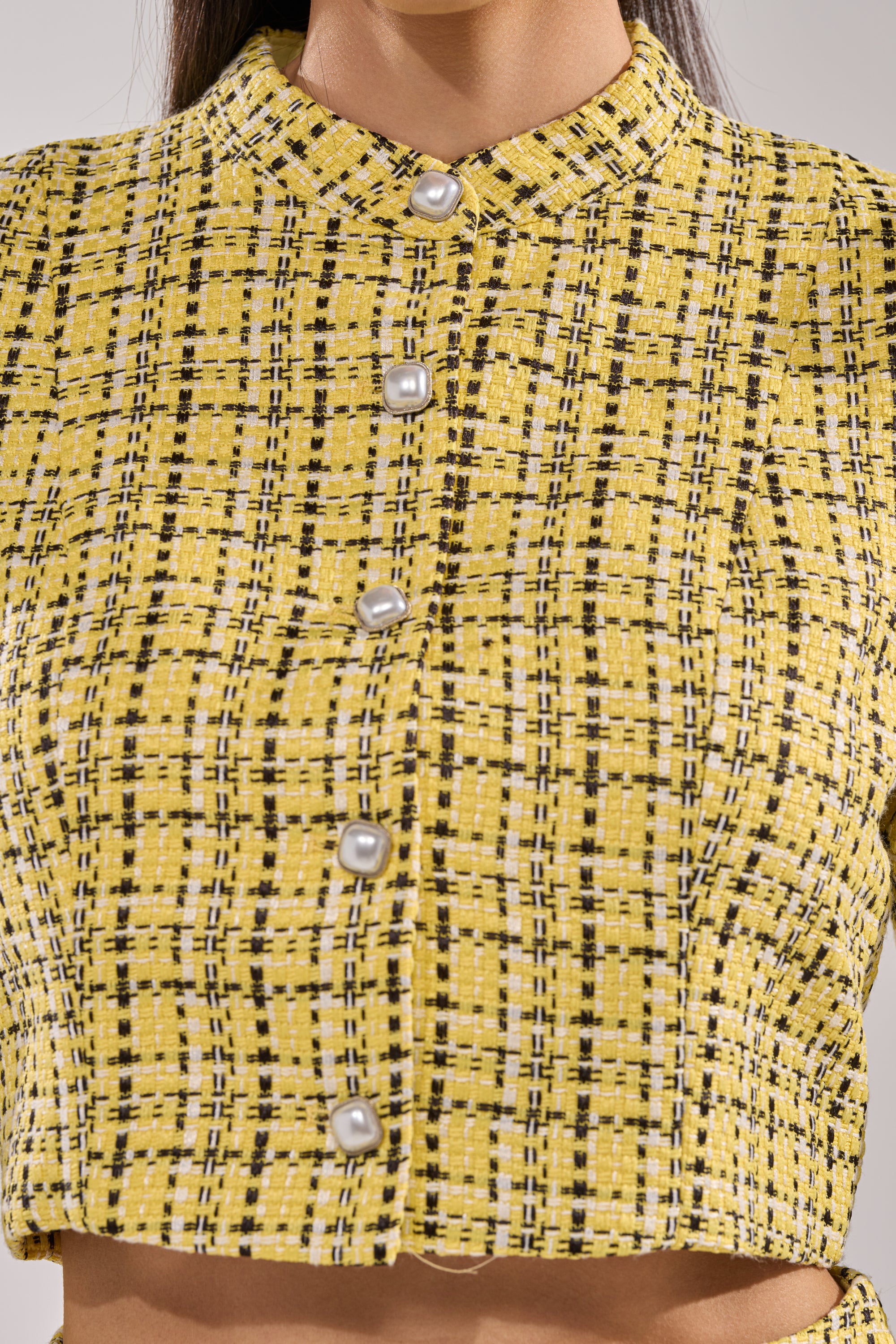 Close-up of a person wearing the FINN TWEED BLAZER—a yellow cropped jacket with a high collar and pearl buttons. Only the neck and upper torso are visible. 8