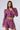 A woman stands against a plain backdrop, modeling a stylish outfit. She is wearing an Effie Tweed Blazer paired with matching high-waisted shorts, embodying Parisian it-girl fashion with the vibrant, textured two-piece set in bold purple, pink, and yellow tweed fabric.