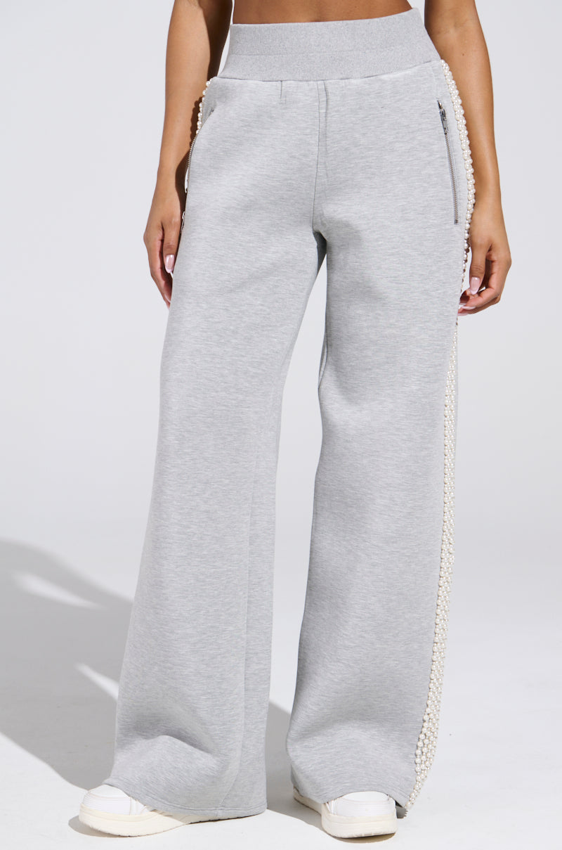 Someone in the PEARL GIRL WIDE LEG JOGGER IN GREY, adorned with pearl embellishments along the seams, stands against a plain white background wearing white sneakers, perfectly embodying athleisure style.