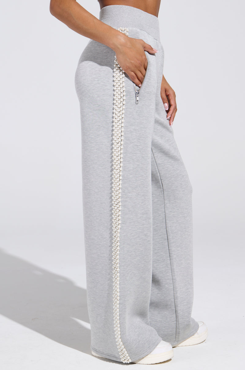 Someone wears gray PEARL GIRL WIDE LEG JOGGER with pearl embellishments on the side seam, creating a soft athleisure vibe, paired with white sneakers and one hand in their pocket.