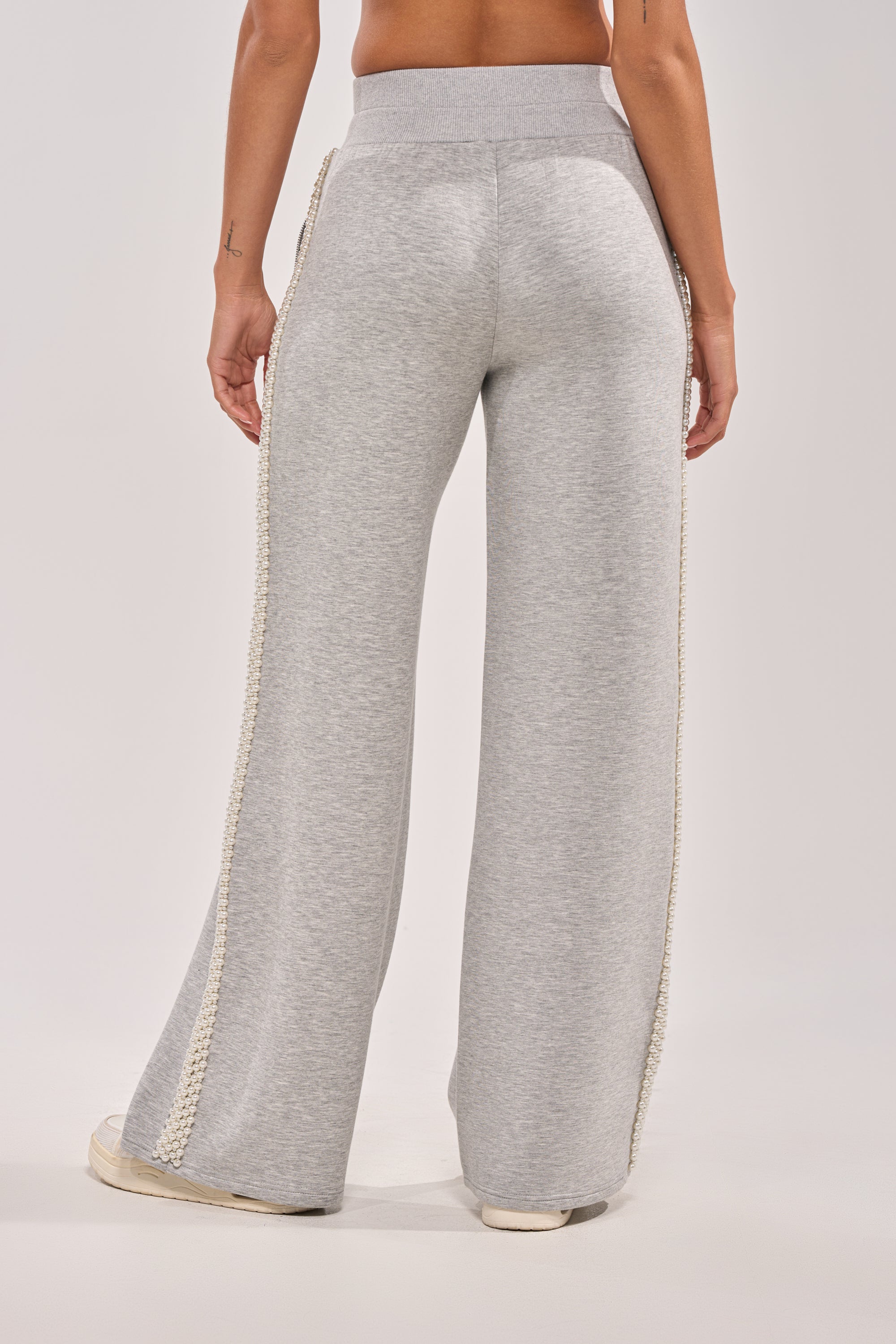 Someone wears the PEARL GIRL WIDE LEG JOGGER IN GREY, featuring a high waist, wide legs, and faux pearl trim along the sides, photographed from behind against a plain background. 5