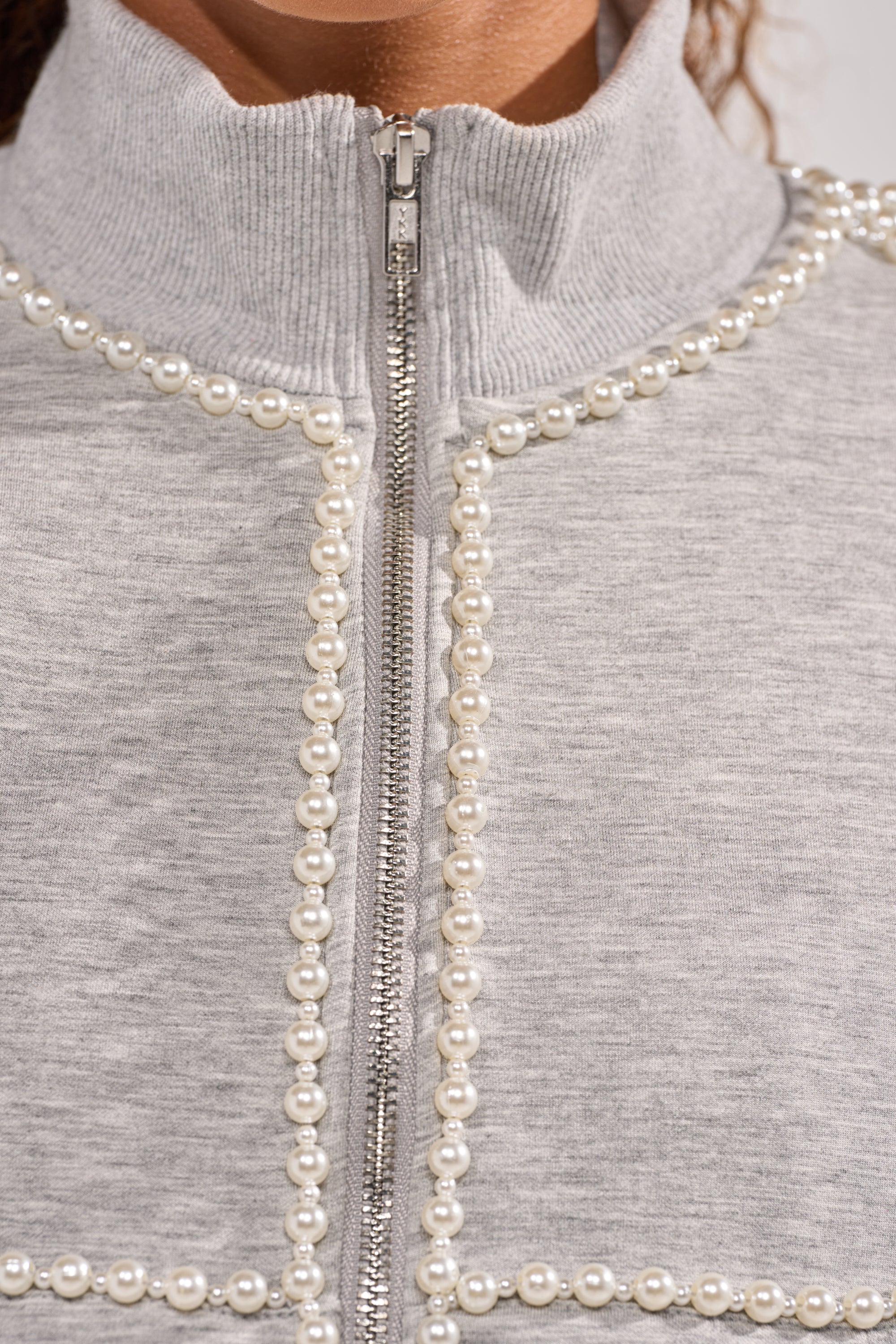 Close-up of the PEARL GIRL ZIP UP SWEATSHIRT IN GREY, featuring pearl embellishments along the zipper and in a square pattern on the front, with an oversized fit and ribbed high collar for added style. 10