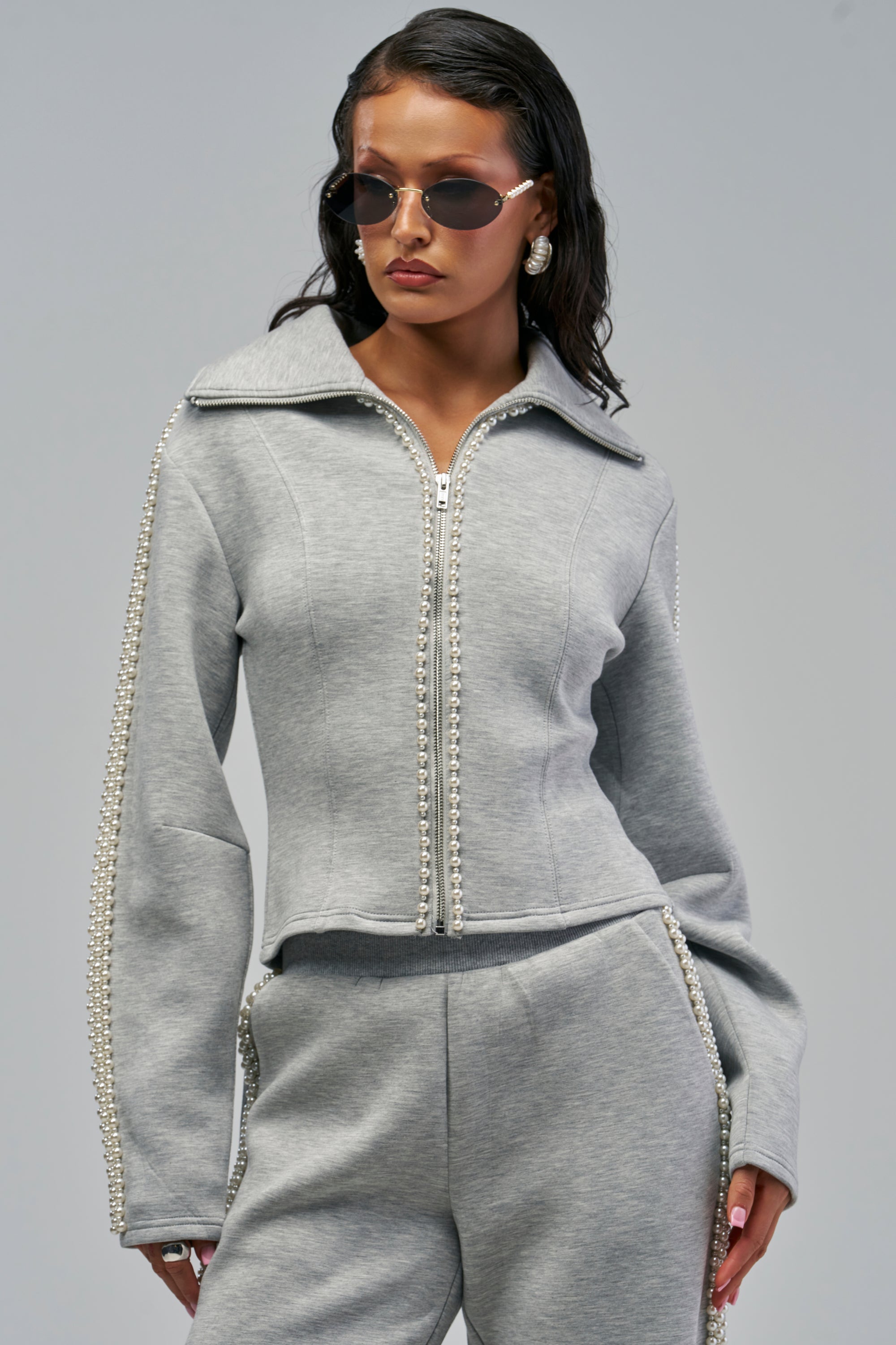 A person wearing a heather grey ALEXA SCUBA ZIP UP SWEATSHIRT, featuring rows of small pearls lining the sleeves and the front zipper.