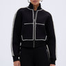 A woman wearing the AKIRA Label PEARL GIRL ZIP UP SWEATSHIRT and matching pants, both featuring rows of white beads. She faces forward with her hair pulled back and accessorizes with large hoop earrings.