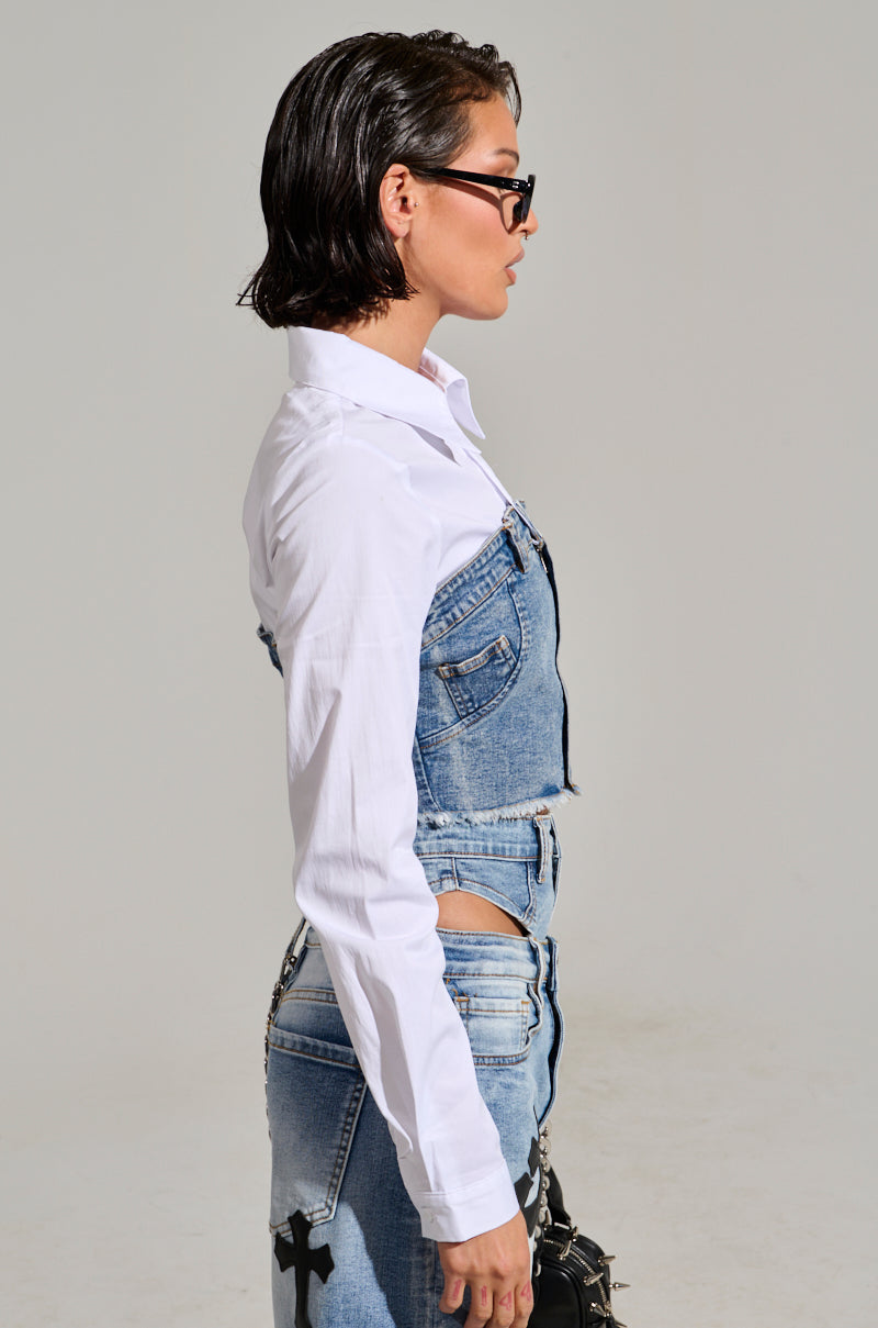 A person with short, wet-looking hair and sunglasses poses in profile against a plain backdrop, dressed in the AKIRA Label's SITTING PRETTY POPLIN & DENIM LONG SLEEVE TOP. The white long sleeves and denim corset finish off their chic look with a contemporary cropped silhouette.