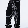 A person is modeling the stylish SPIDER SEQUIN DETAIL JOGGER, featuring an abstract silver spiderweb pattern, paired with black high-heeled ankle boots against a plain white studio background.