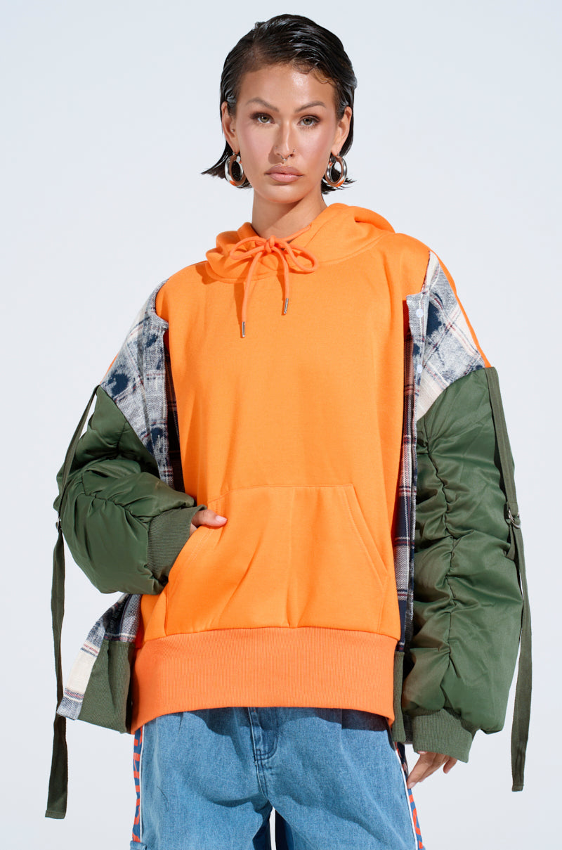 A person with short, slicked-back hair models the MY EX IS MY BIGGEST FAN REBUILT SWEATSHIRT with an oversized fit, layered under a green plaid jacket and styled with blue jeans, posing against a plain light background. 0