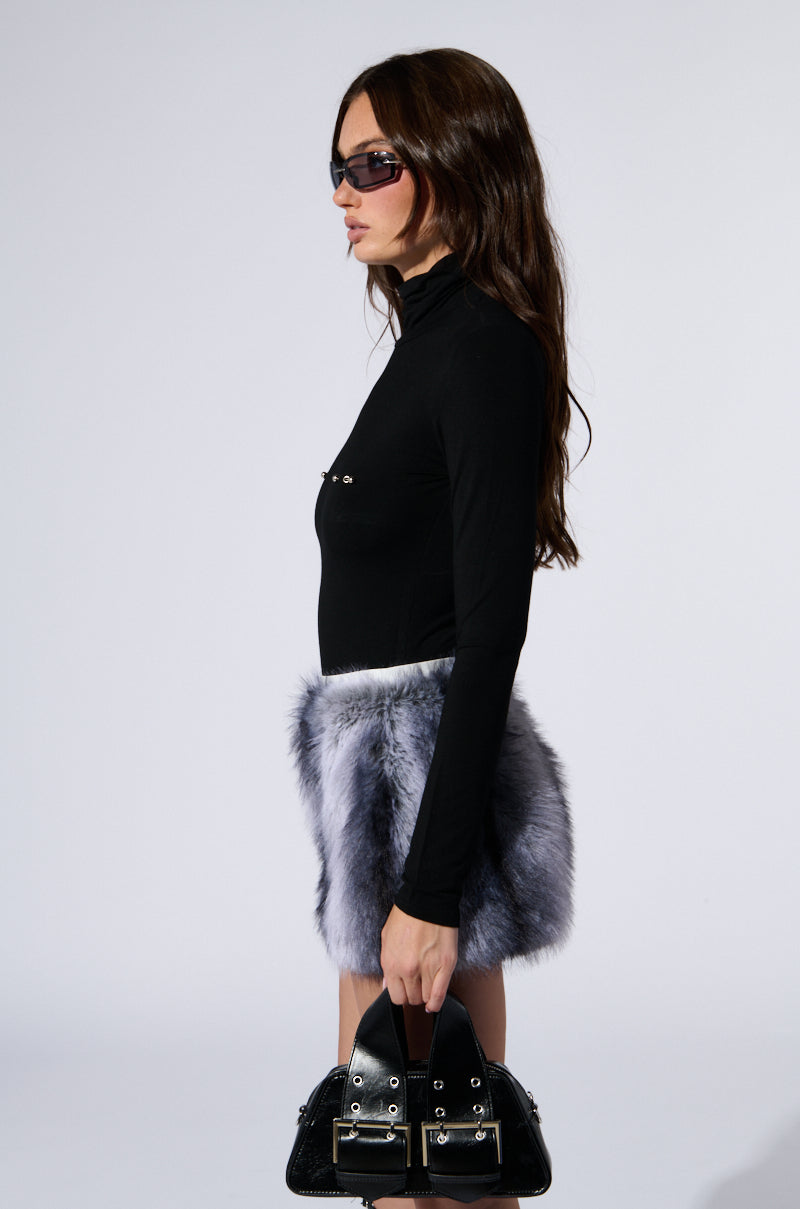 A woman with long brown hair wearing sunglasses and the QUIT STARING LONG SLEEVE BODYSUIT IN BLACK is holding a black handbag. She is wearing a faux fur gray skirt with industrial bar piercing embellishments and standing against a plain white background.