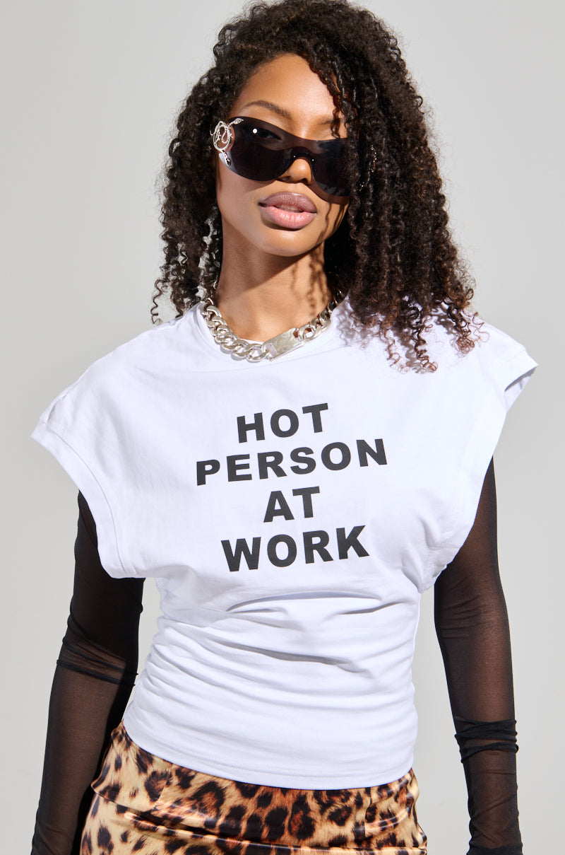 A woman with curly hair flaunts a bold look, wearing large sunglasses and a cropped silhouette. She pairs her "HOT PERSON AT WORK LONG SLEEVE GRAPHIC SHIRT" with leopard print pants. Her confident expression is enhanced by a chunky necklace, completing the stylish ensemble.