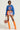 A person stands confidently, wearing a blue "Chicago Athletic" cropped relaxed fit sweatshirt, a vibrant mini skirt with a basketball design, and knee-high orange boots. They accessorize with sunglasses, a necklace, and hold a basketball in a netted bag.