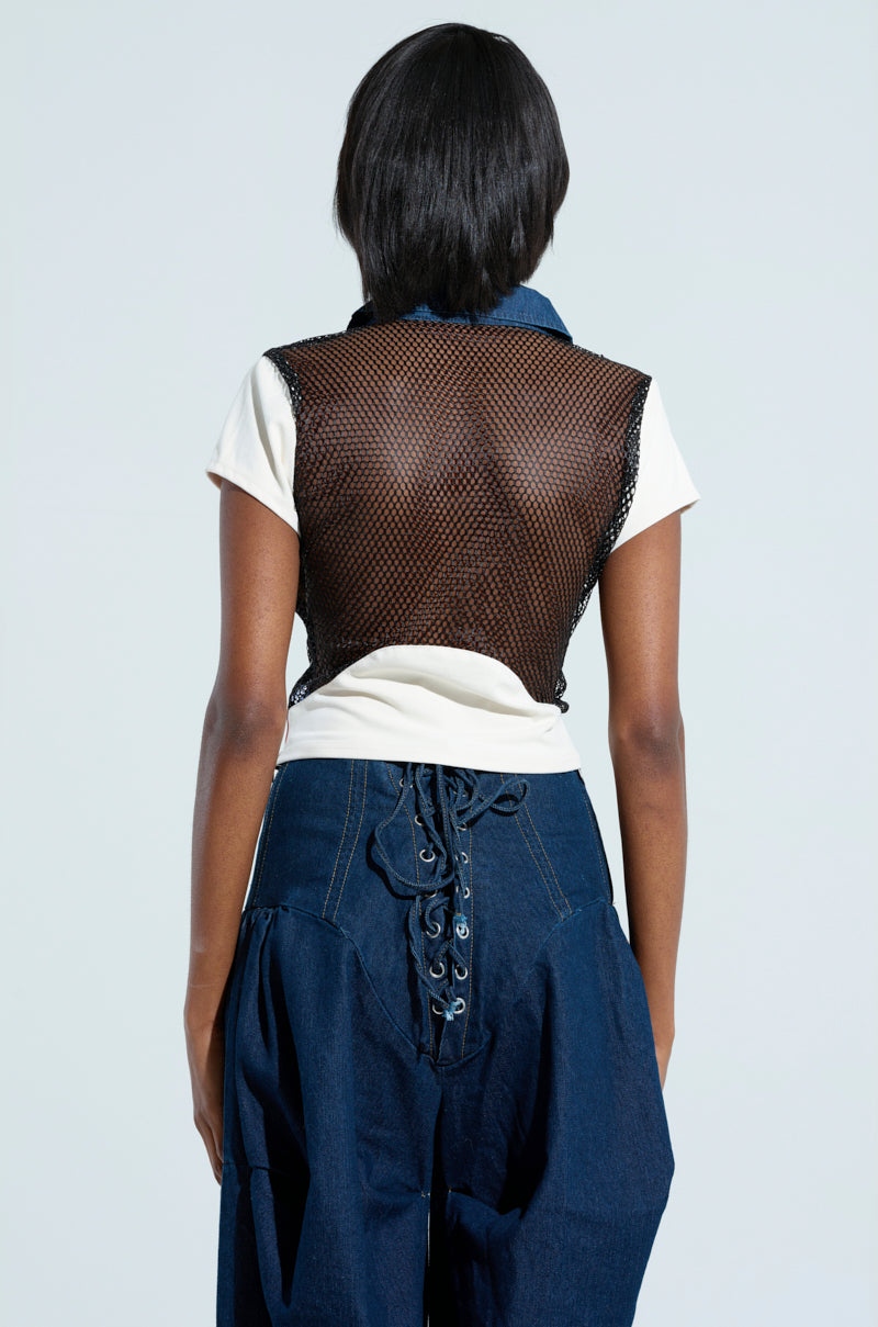 A person with dark hair is seen from behind wearing a white shirt layered over an Edgy Diva Short Sleeve Netted T-shirt, and a black fishnet vest, paired with dark blue pants featuring a lace-up design. The background is plain and light-colored.
