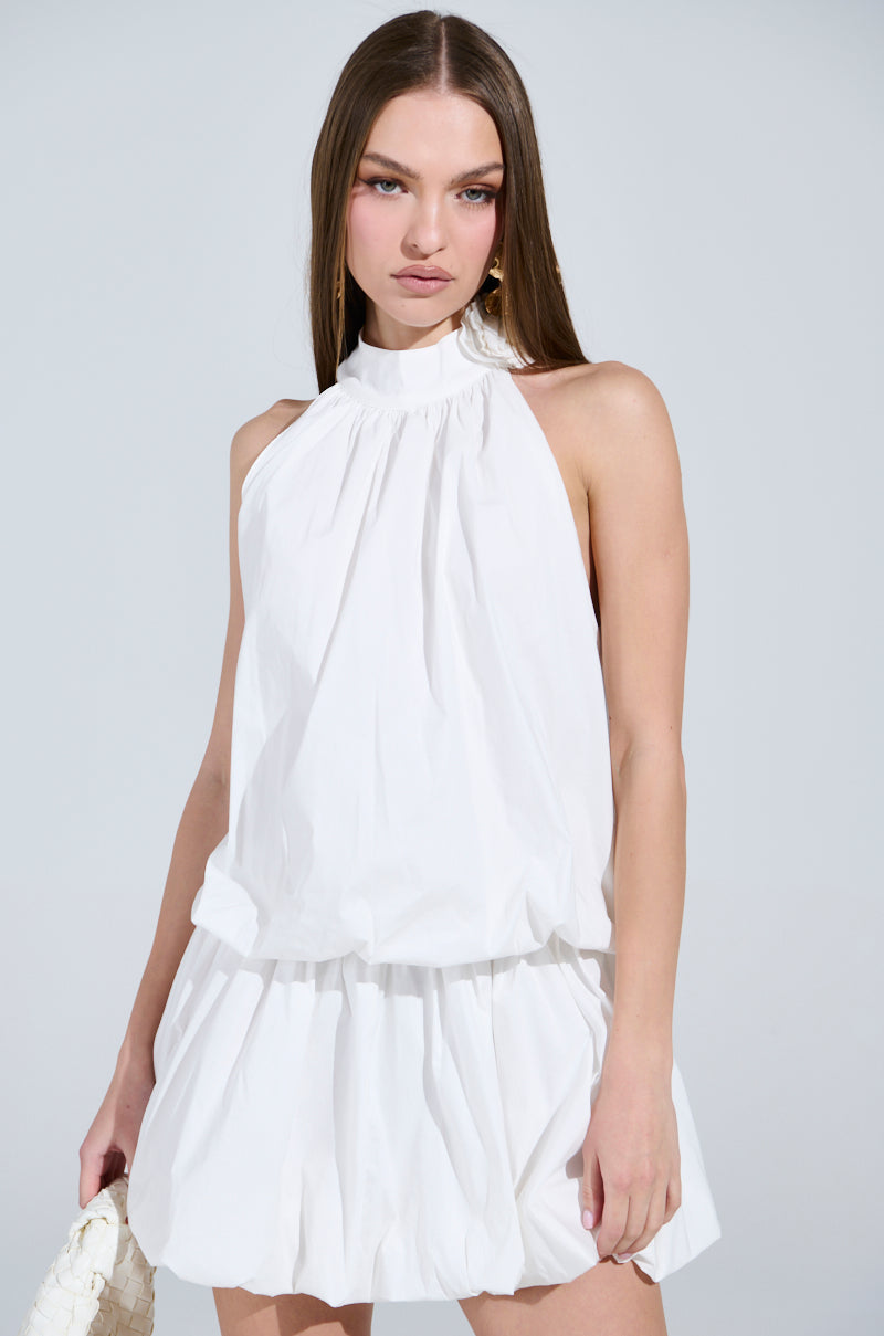 Wearing the "Dressed for Any Occasion" white poplin mini dress with ruched waist and skirt, a person with long brown hair holds a textured white handbag against a plain gray backdrop.
