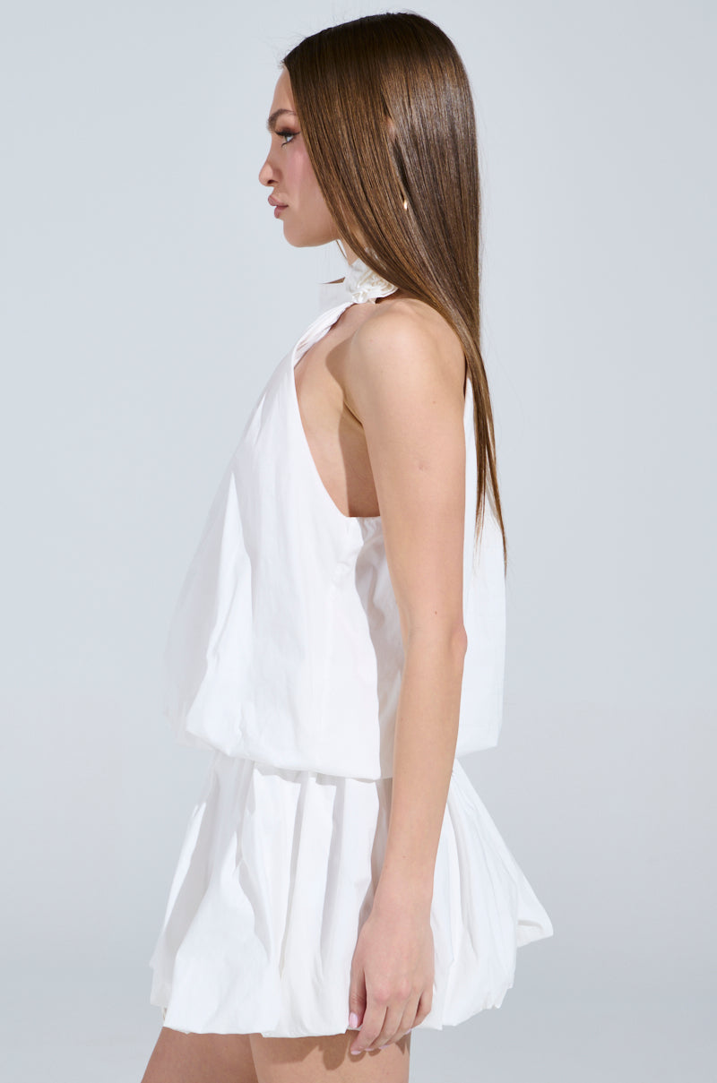 A stylish woman in profile, with long hair flowing over the "Dressed for Any Occasion" white poplin mini dress featuring ruched detail, stands confidently against a plain gray backdrop.