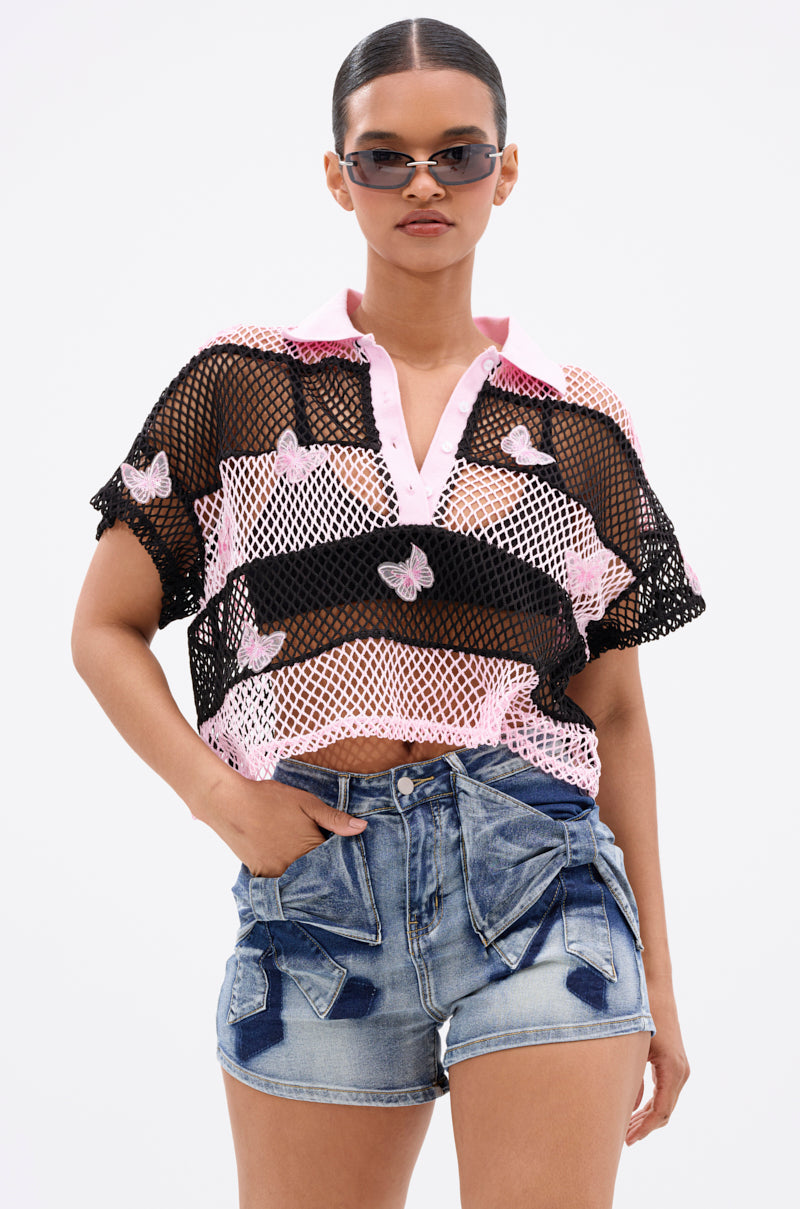 A woman poses confidently in the FLY WITH ME STRIPE OVERSIZED TEE—lightweight and breathable with black and pink mesh, beaded 3D butterfly appliqués—paired with denim shorts, against a plain white background.