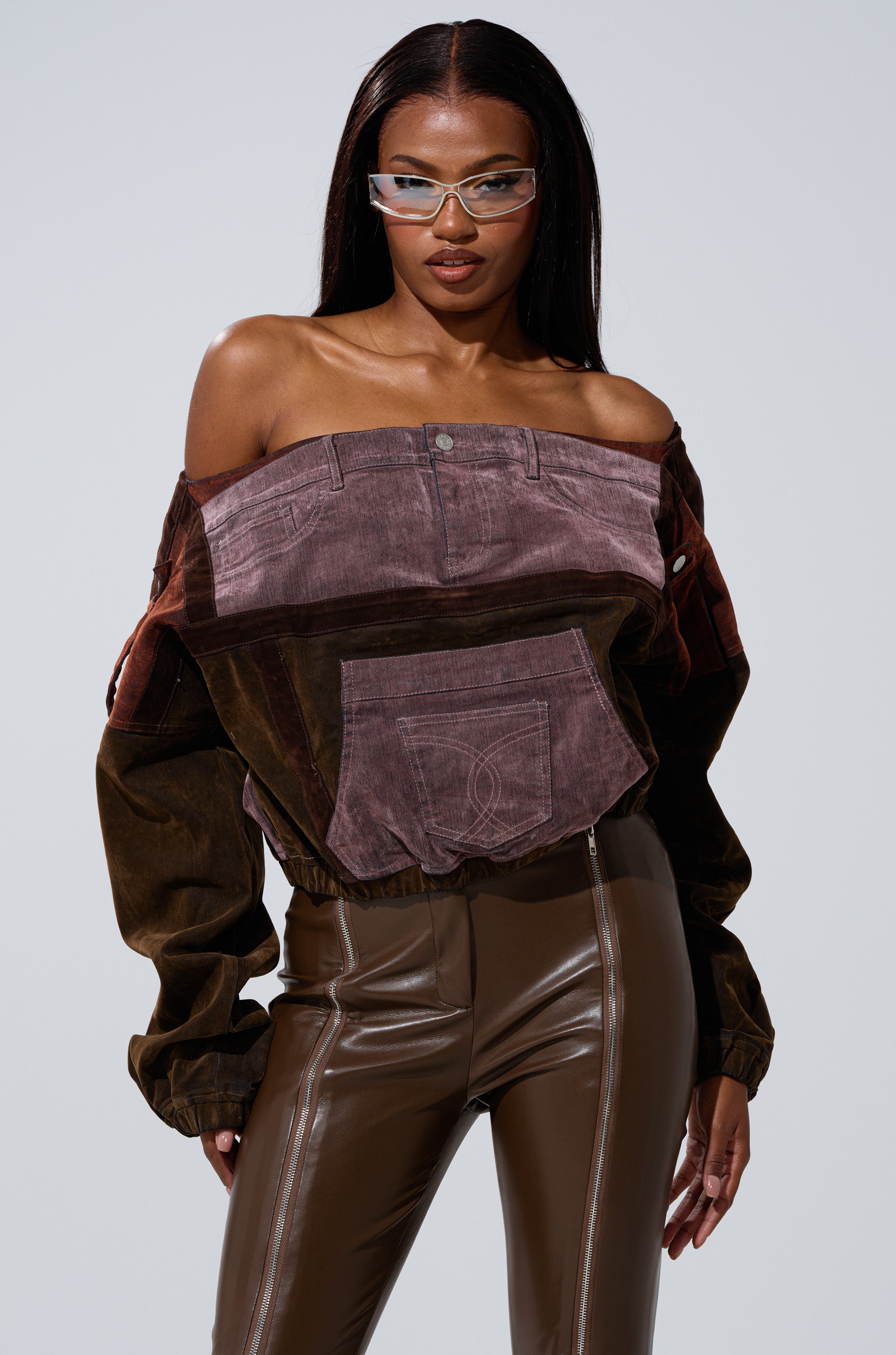 A woman wears the PATCH ME UP MINERAL WASHED SWEATSHIRT IN PURPLE, paired with high-waisted brown leather pants. She has long straight hair, clear-framed sunglasses, and a confident expression. 0