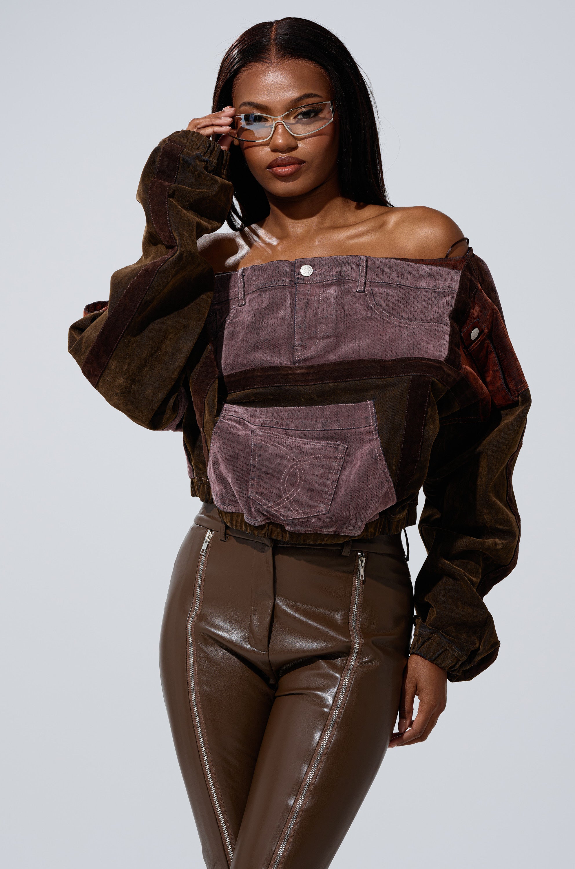 A woman confidently poses in the PATCH ME UP mineral washed purple sweatshirt with denim patchwork, pairing it with stylish brown leather pants, front zippers, and clear-framed glasses. 1