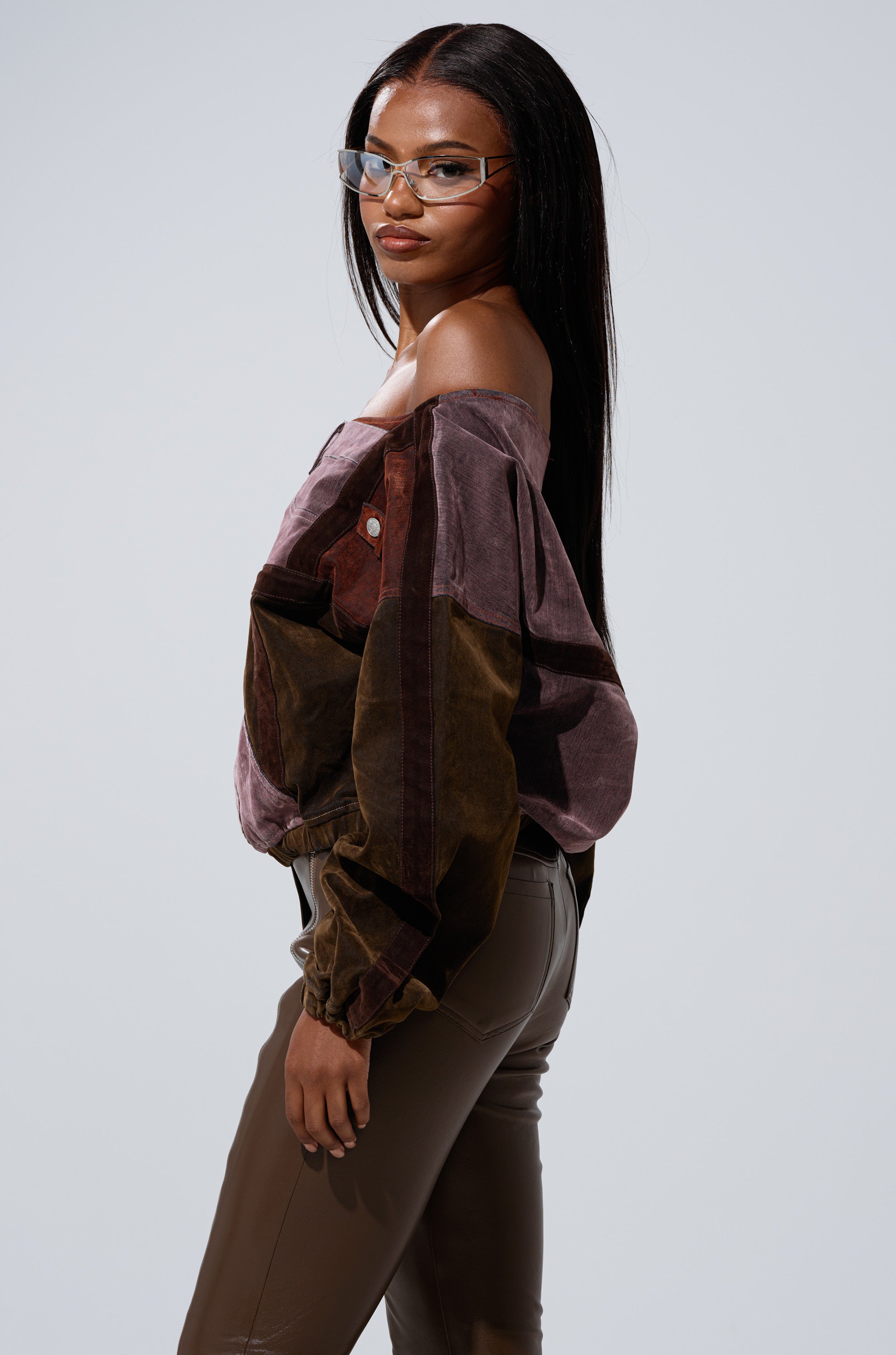 A woman with long straight hair and clear-frame glasses wears the PATCH ME UP MINERAL WASHED SWEATSHIRT IN PURPLE, featuring voluminous sleeves, as she stands in profile against a plain light gray background. 2
