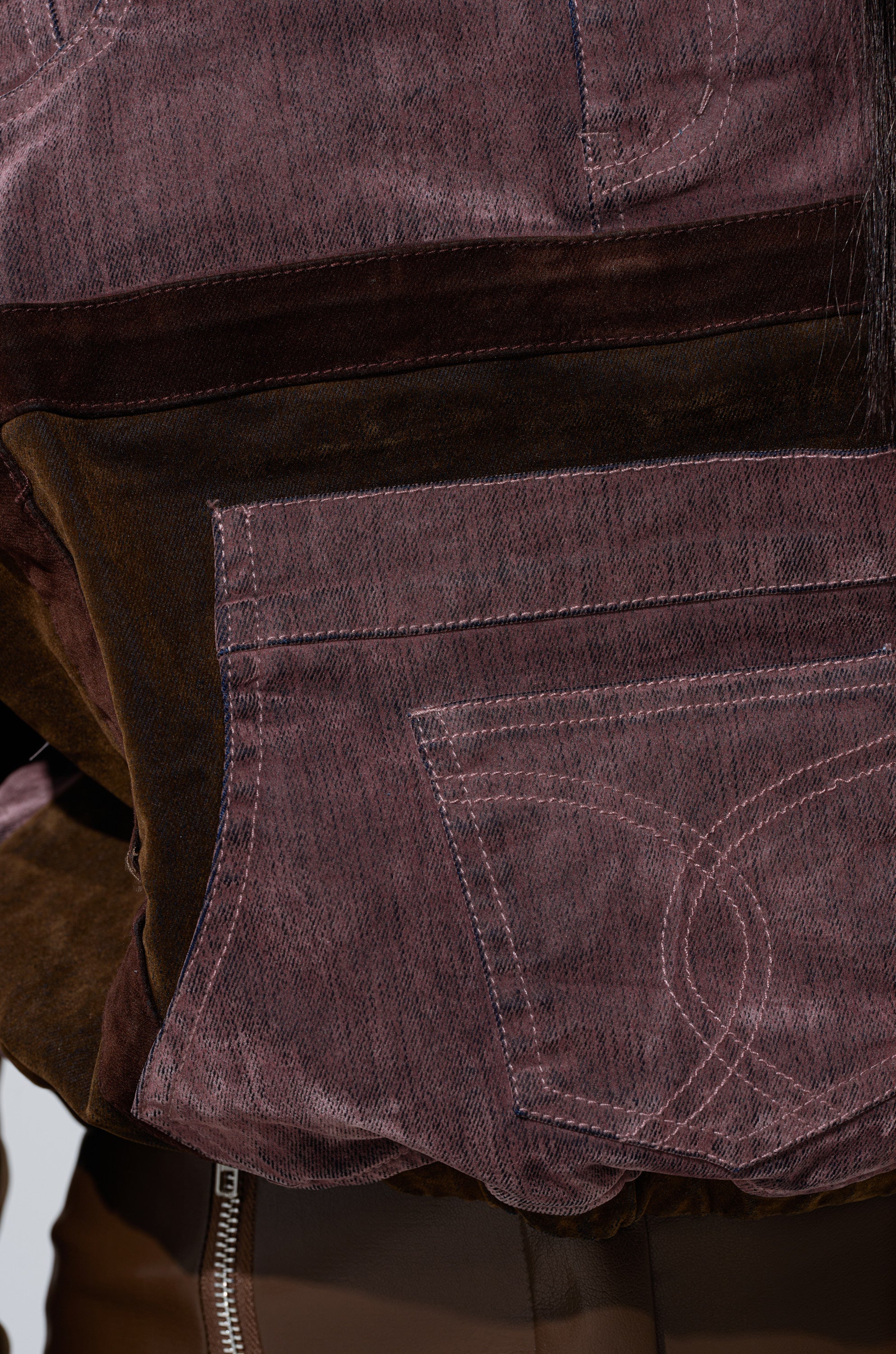 Close-up of a person wearing the PATCH ME UP MINERAL WASHED SWEATSHIRT IN PURPLE, featuring visible light pink stitching and geometric patchwork details, paired with brown pants with zipper detail. 5