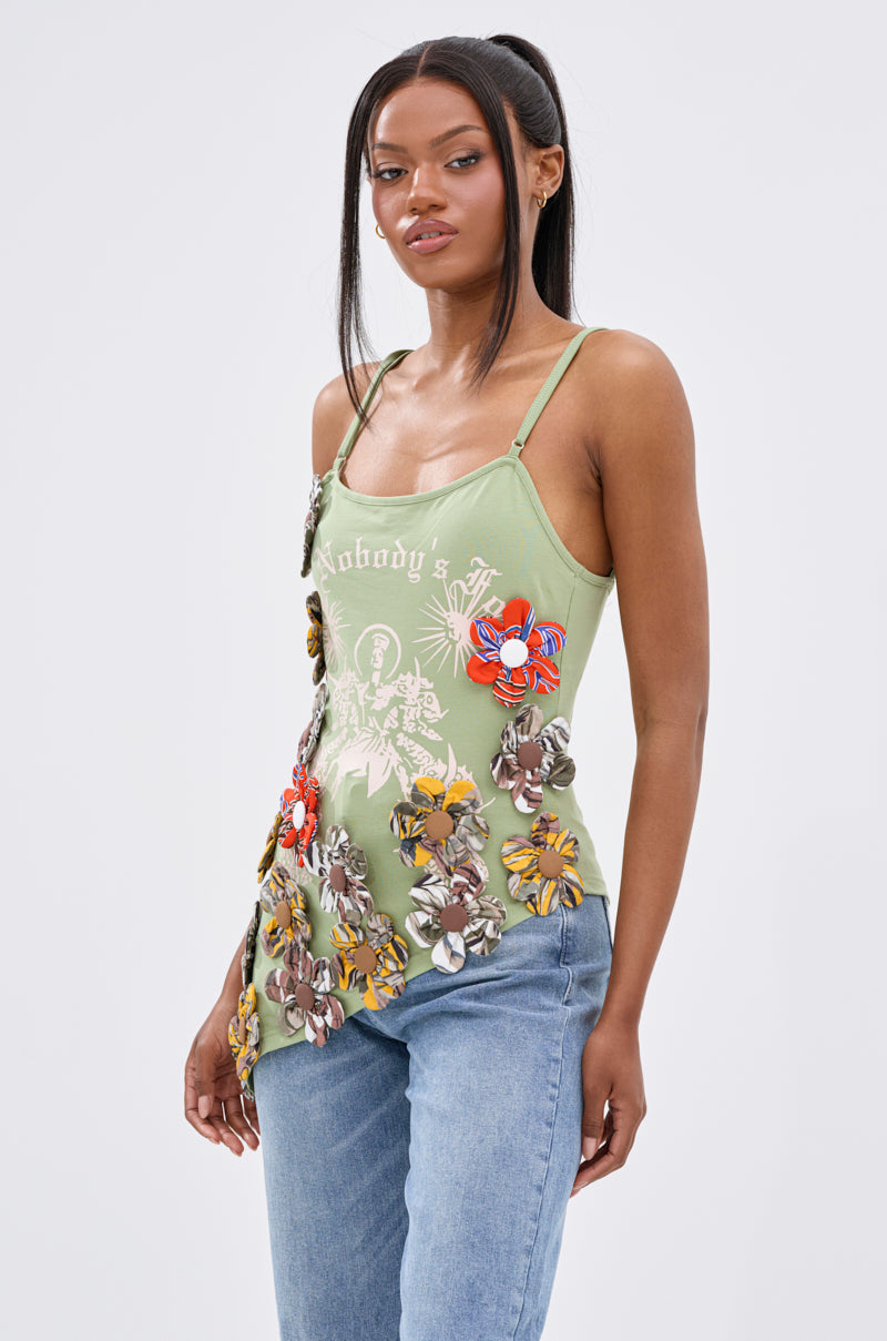 A woman with long dark hair wears the FOR THE FREE FLORAL EMBELLISHED TOP in light green with blue jeans, standing against a plain white background and embodying confident Bohemian Chic style.
