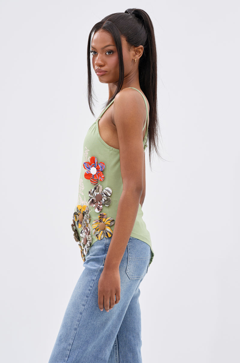 A woman with long straight hair in a high ponytail wears the FOR THE FREE FLORAL EMBELLISHED TOP and light blue jeans, standing sideways against a plain light background.