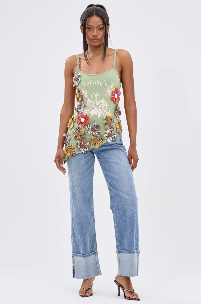 A woman with long, straight hair and a neutral expression faces forward against a white background, wearing the FOR THE FREE FLORAL EMBELLISHED TOP in light green stretchy cotton, light blue cuffed jeans, and heeled sandals.